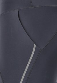 Leggings blu navy realizzati in tessuto elastico con un design elegante. Presentano un taglio a triangolo e una striscia riflettente grigia lungo la cucitura.