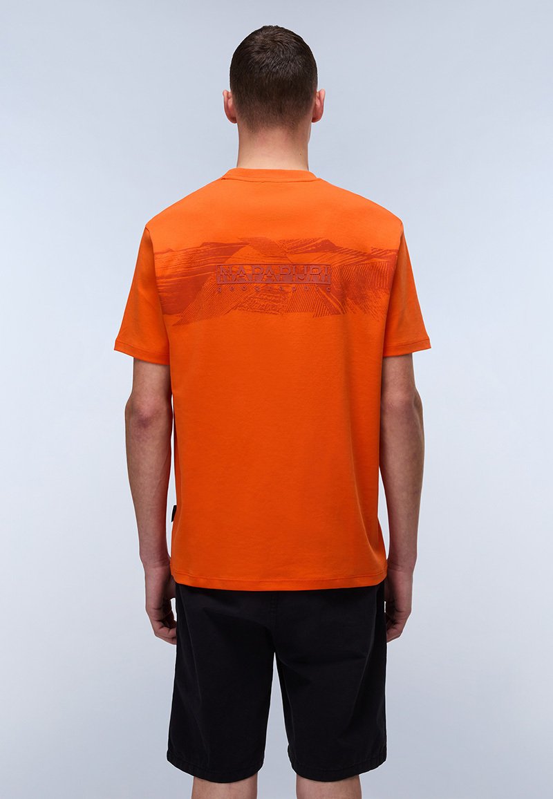 Orange bomulds t-shirt med korte ærmer, der har et tekstureret grafisk design på ryggen, parret med sorte shorts.
