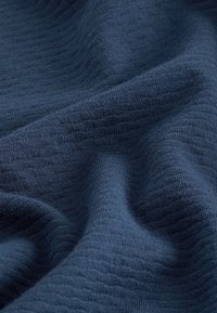 Gestructureerde donkerblauwe stof met een geribbeld patroon, met zachte plooien en kreuken die duiden op zachtheid en rekbaarheid.