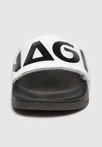 Chancla de tira ancha en blanco y negro con letras negras en un fondo blanco, suela negra texturizada y diseño minimalista.