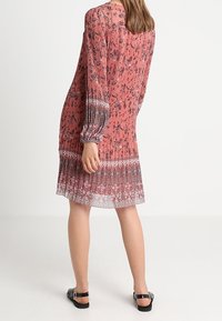 Vestido de manga larga, rosa con flores, con un dobladillo estampado y detalles de pliegues. Hecho de tela ligera. Usado con sandalias negras.