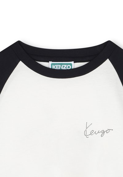 T-shirt à manches courtes avec un corps blanc et des manches raglan noires. Présente un logo "Kenzo" à pois sur le devant. Fabriqué en coton doux.