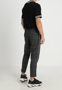 Černé krátké tričko polo s bílými pruhy, zkombinované se šedými vzorovanými slim-fit kalhotami s bočním bílým pruhy a černými teniskami.