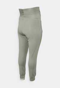 Calças de jogging verde claro com uma cintura alta, tecido elástico, bolsos laterais e punhos afunilados nos tornozelos. Textura suave.