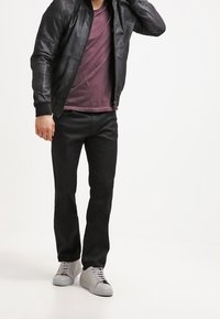 Chaqueta bomber de cuero negro, camiseta burdeos, pantalones negros y zapatillas gris claro, mostrando un estilo casual y ajustado.