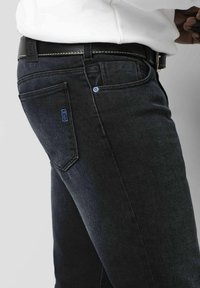 Dunkelblaue Jeans im taillierten Design, mit einem blauen Markenetikett an der Gesäßtasche und einem schwarzen Gürtel mit kontrastierender Naht.