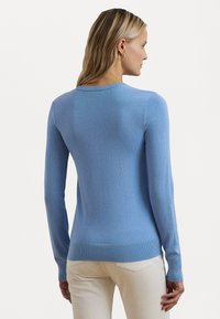 Šviesiai mėlynas megztinis, pagamintas iš minkštos medžiagos, su ilgomis rankovėmis, apvaliu iškirpimu ir brauktais rankogaliais bei apvadu. Matomų raštų ar akcentų nėra.