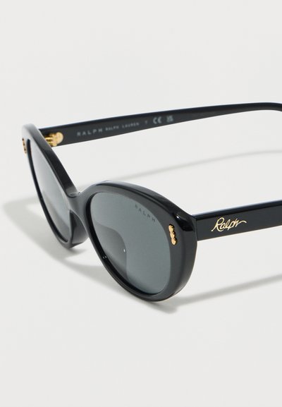 Μαύρα στρογγυλά γυαλιά ηλίου με σκούρους φακούς και χρυσή σήμανση «Ralph» στην πλευρά και κοντά στη άρθρωση, σε λευκό φόντο.
