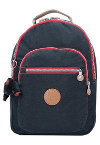 Navy backpack with red accents, zippered pockets, and a furry monkey keychain. Features a circular leather logo patch on the front.