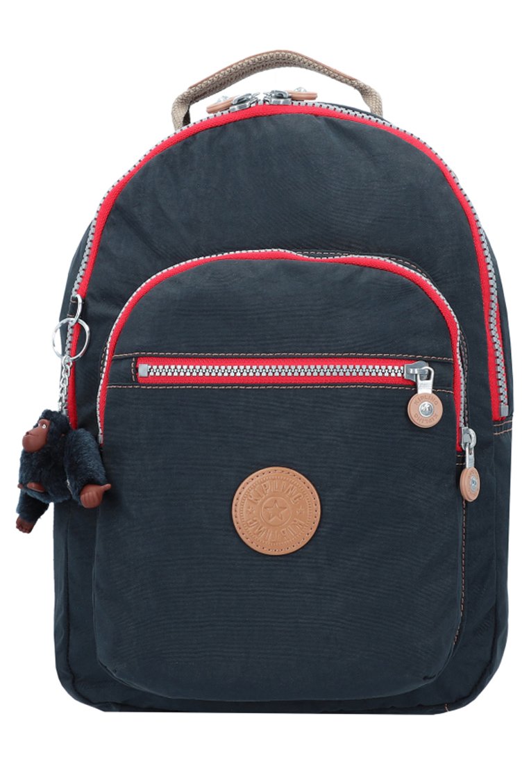 Navy backpack with red accents, zippered pockets, and a furry monkey keychain. Features a circular leather logo patch on the front.