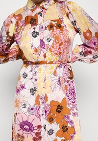 Mønstret blomsterkjole i flere farver med knaplukning foran, krave og belted talje. Fremstillet i let stof med forskellige blomsterprint i pink, orange og gult.