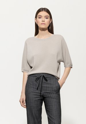 Beige Stricktop mit rundem Halsausschnitt und kurzen, lässigen Ärmeln, kombiniert mit dunkel gestreiften Hosen mit Kordelzugbund.