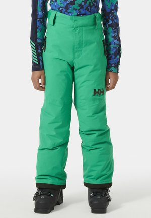 Pantalones de esquí impermeables verdes con cintura ajustable, bolsillos laterales y puños elásticos; combinados con botas de esquí negras.