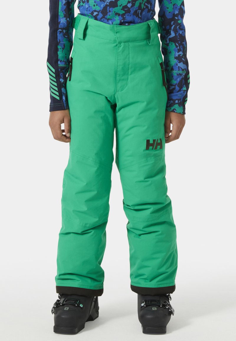 Zelené nepromokavé lyžařské kalhoty s nastavitelným pasem, bočními kapsami a elastickými manžetami; doplněné černými lyžařskými botami.