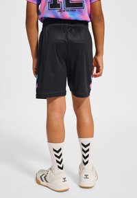 Svarta träningstights tillverkade av lätt material, med en avslappnad passform och färgglada sidodelar. Bärs med vita strumpor och sneakers.