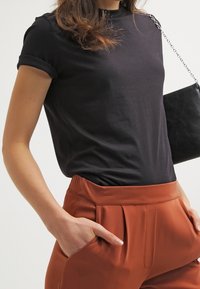 Camiseta de algodón negra con mangas enrolladas, combinada con pantalones anaranjados con pliegues y un pequeño bolso de cuero negro con una correa de cadena.