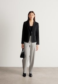 Mustast nööbiga jakk, hallid kohandatud püksid ja mustad teravate ninadega kingad. Aksessuaaride hulka kuulub väike must käekott.