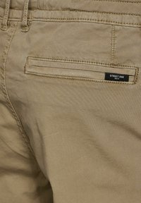 Karakullbyxor i bomull med en slimmad design, med en bakficka och en svart etikett med texten "STREET ONE MEN." Slät textur och rena stygn.