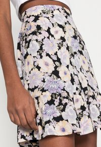 Kukkamekko mustasta kankaasta, jossa on pastellivärisiä kukkia ja vihreyttä; levenevä malli, jossa on poimutettu helma.