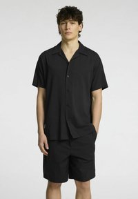 Camicetta nera a maniche corte con bottoni e pantaloni abbinati, caratterizzati da una trama liscia e da un design con colletto classico. Aspetto semplice e minimalista.