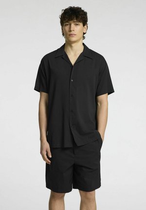 Camicetta nera a maniche corte con bottoni e pantaloni abbinati, caratterizzati da una trama liscia e da un design con colletto classico. Aspetto semplice e minimalista.