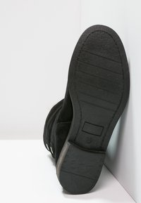 Botas de ante negras con suela de goma texturizada. Presentan una forma plana, costuras laterales y un logotipo sutil en la suela.