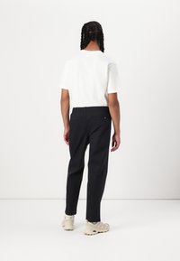 White crew neck t-shirt paired with navy trousers featuring an elastic waistband and back pockets; worn with light-colored sneakers.