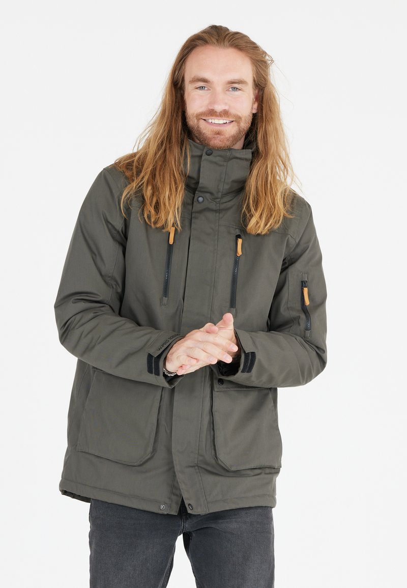 Jacket impermeabile verde scuro con colletto alto, due tasche frontali, cerniere nere e dettagli in pelle marrone sui tiranti.