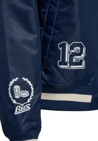 Manche de veste bleu marine avec logo blanc "Bee's" représentant un verre de bière et un burger, et un grand "12" blanc sur le corps de la veste.