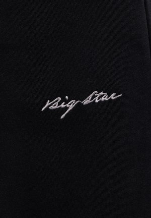 Broderie cursive blanche "Big Star" sur tissu noir, montrant la texture détaillée du tissu et des coutures.