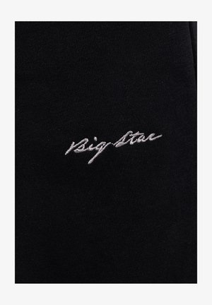 Białe, kursywne haftowane napisy "Big Star" na czarnej tkaninie, ukazujące szczegółową teksturę materiału i szwów.