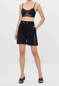 Černý krajkový bralet a černé bavlněné šortky s elastickým pasem. Šortky mají postranní kapsy a dekorativní steh na levé noze.