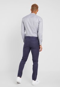 Ljusblå skjorta med knäppkrage, kombinerad med slim-fit marinblå byxor med ett vitt rutmönster, avslutat med vita sneakers.