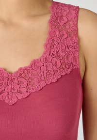 Canotta rosa con colletto in pizzo testurizzato, corpo morbido e design a girocollo, che mette in mostra un tessuto morbido ed elastico.