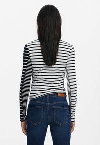 Langarmshirt mit schwarz-weißen Horizontalstreifen; taillierte Passform. Kombiniert mit dunkelblauen Jeans, die ein Label am Bund haben.