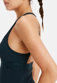 Camiseta de entrenamiento en color navy con escote redondeado y tirantes finos, que presenta una banda texturizada con el nombre de la marca y un diseño de espalda descubierta.