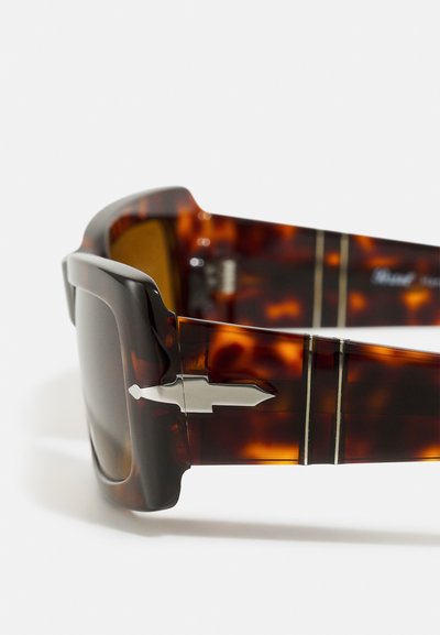 Óculos de sol em tartaruga castanha com armações grossas, lentes escuras e detalhes metálicos nas hastes. Acabamento texturizado com detalhes de design sofisticados.