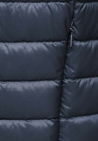 Sezione di giacca a vento blu scuro con texture trapuntata e imbottita, dotata di tasca con zip e superficie liscia e resistente all'acqua.