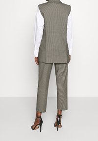 Grau karierter Weste und passender Hose, getragen mit einem weißen Hemd. Abgerundet mit schwarzen hochhackigen Sandalen und minimalem Schmuck.