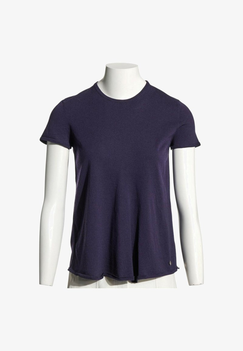 T-shirt bleu marine à manches courtes et col rond sur un torse de mannequin blanc avec pantalon blanc, fond uni.