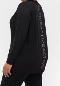 Zwarte langemouwen sporttop met een relaxte pasvorm. Kenmerkend zijn de verticale witte tekst "ACTIVE" aan de zijkant en de zachte, ademende stof.