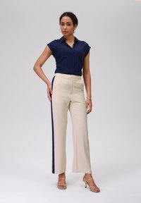 Marineblauwe overhemd met korte mouwen en kraag, met voorzakken, gecombineerd met beige wijde broek met marineblauwe zijstrepen. Glad materiaal, slim fit.