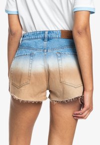 Pantalones cortos de mezclilla con un efecto ombré que va del azul claro al beige, dobladillo deshilachado, bolsillos traseros y una etiqueta de cuero marrón con la marca en la cintura.