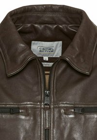 Bruine leren jas met een ritssluiting, een brede kraag en twee met rits afgesloten zakken. "Camel Active" label zichtbaar aan de binnenkant. Soepele textuur.