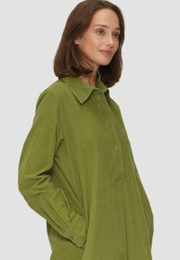 Grünes Cordhemd mit Hemdkragen, langen Ärmeln und knöpfbaren Manschettendetails, das einen entspannten, übergroßen Schnitt und eine subtile Textur aufweist.