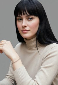 Silverarmband på ett handled, med sammanflätade, delikata länkar. Modellen bär en ljusbeige polotröja med ribbade muddar och en slät textur.