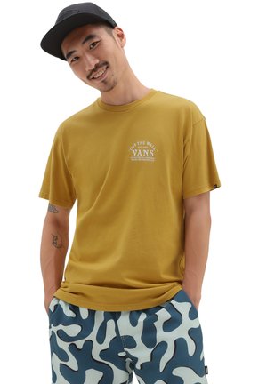 Camiseta de manga corta color mostaza con logo impreso en blanco, combinada con pantalones cortos de camuflaje en tonos azul y azul claro. Diseño simple y casual.