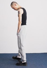 Black ribbed tank top, gray sweatpants with waistband and Champion logo, and black shoes. Model in a side profile stance.