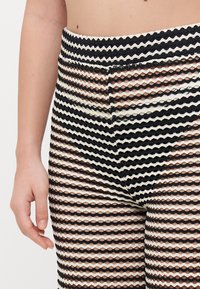 Leggings in rete a righe bianche e nere che presentano un motivo a maglia aperta testurizzato con una cintura larga, caratterizzati da un design a strati.