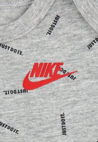 Siva pamučna majica s istaknutim crvenim Nike logotipom i crnim uzorkom teksta "JUST DO IT" po cijeloj tkanini.